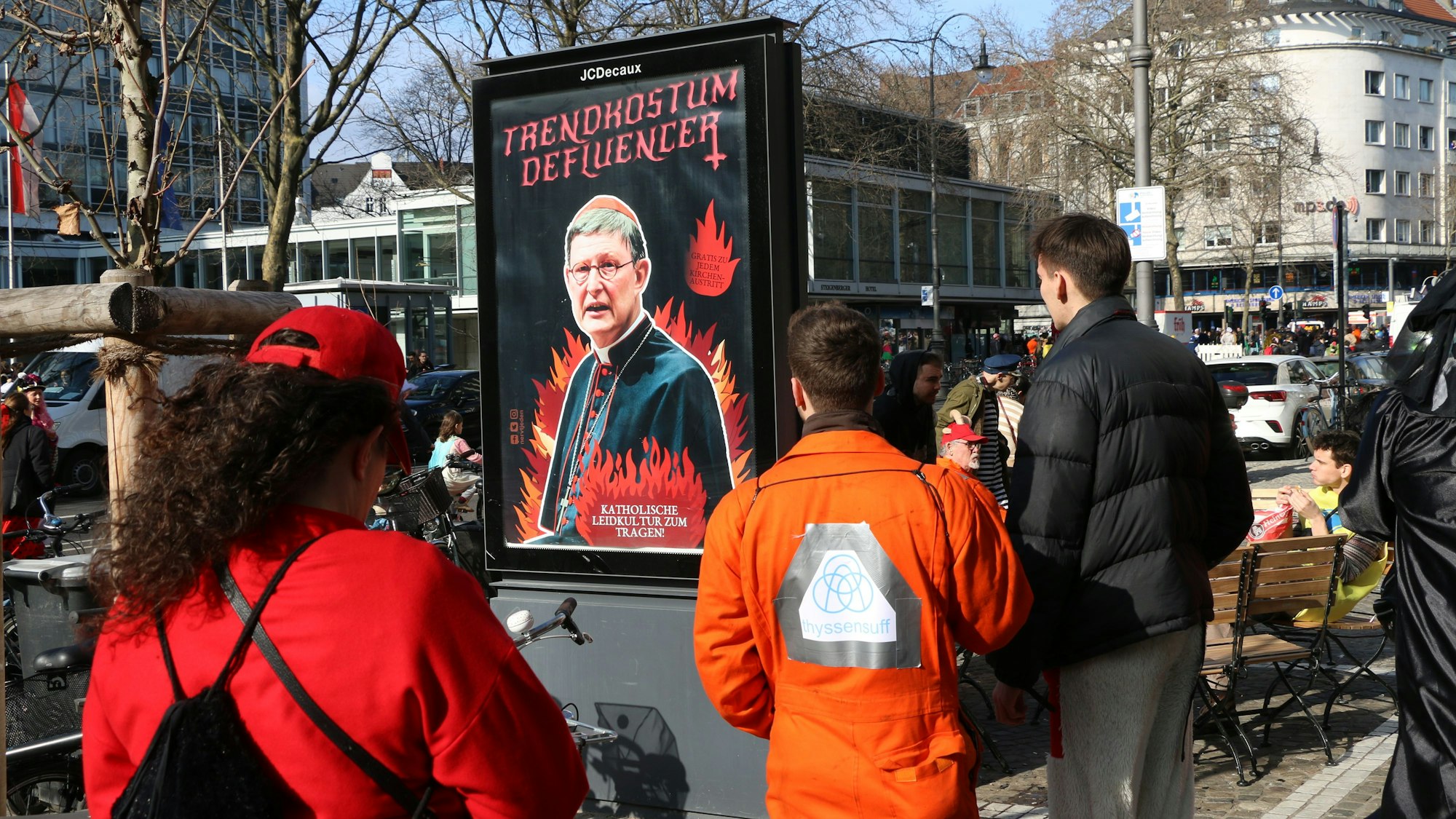 Plakataktion im Karneval: Jecke beobachten am Rosenmontag in Köln die Plakate, die sich gegen Kardinal Woelki und das Kölner Erzbistum richten.