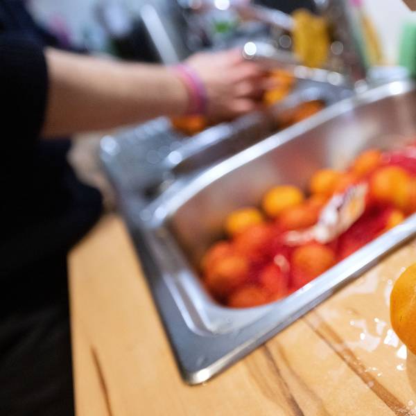 Einzelne schimmelige Mandarinen liegen aussortiert auf einer Küchenarbeitsplatte, während eine Frau andere unverdorbene Mandarinen wäscht.