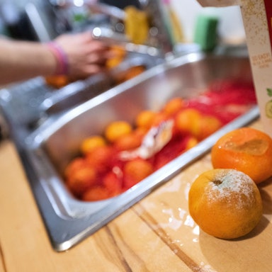 Einzelne schimmelige Mandarinen liegen aussortiert auf einer Küchenarbeitsplatte, während eine Frau andere unverdorbene Mandarinen wäscht.