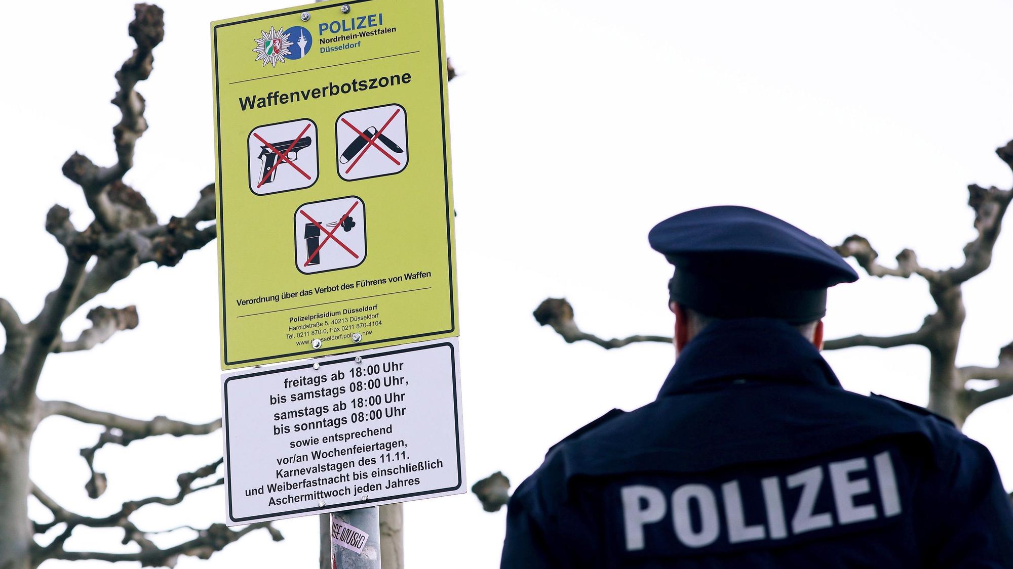 Ein Polizist steht auf der Düsseldorfer Rheinufer-Promenade vor einem Schild zur Waffenverbotszone.