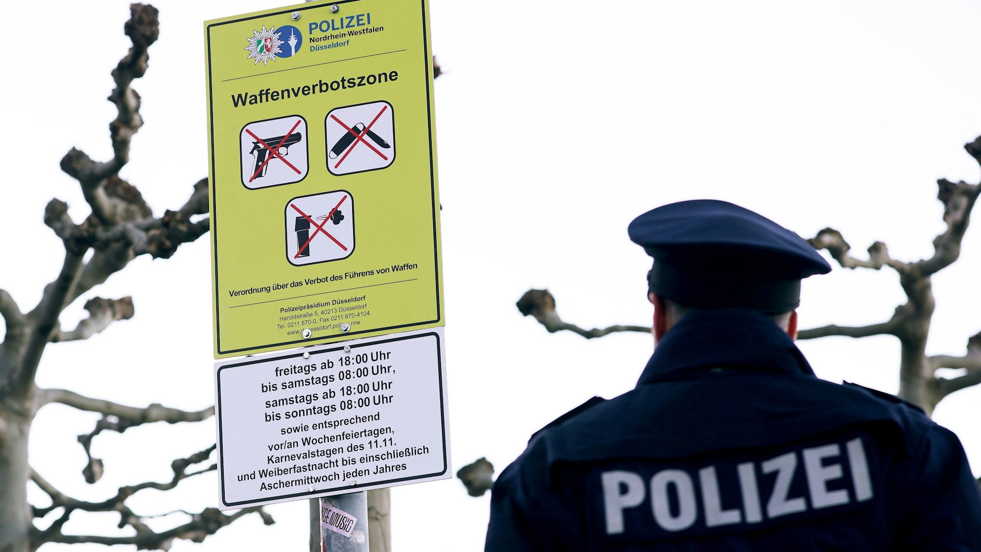 Ein Polizist steht auf der Düsseldorfer Rheinufer-Promenade vor einem Schild zur Waffenverbotszone.