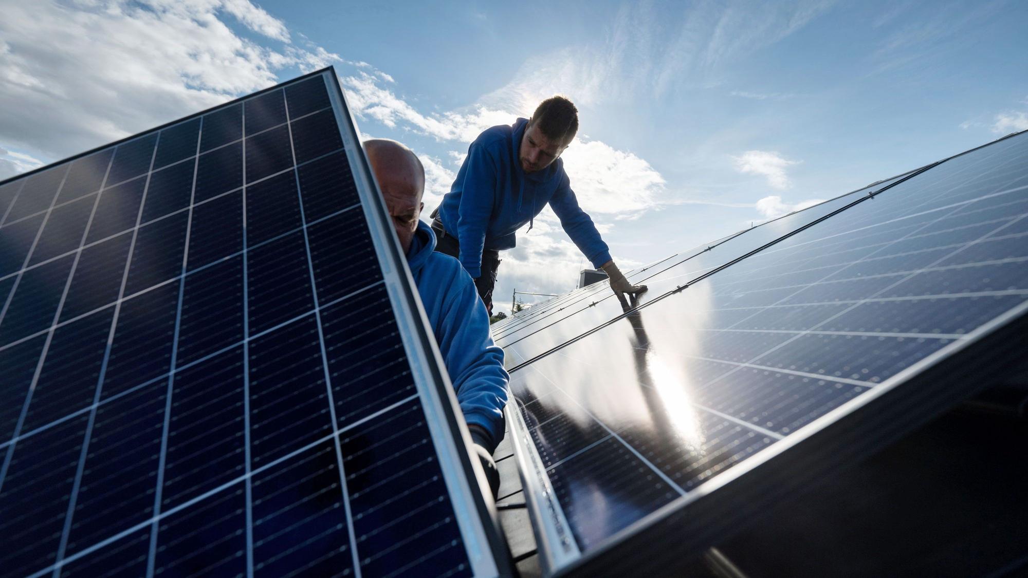 Zwei Männer montieren Photovoltaikmodule auf dem Dach eines Wohnhauses.