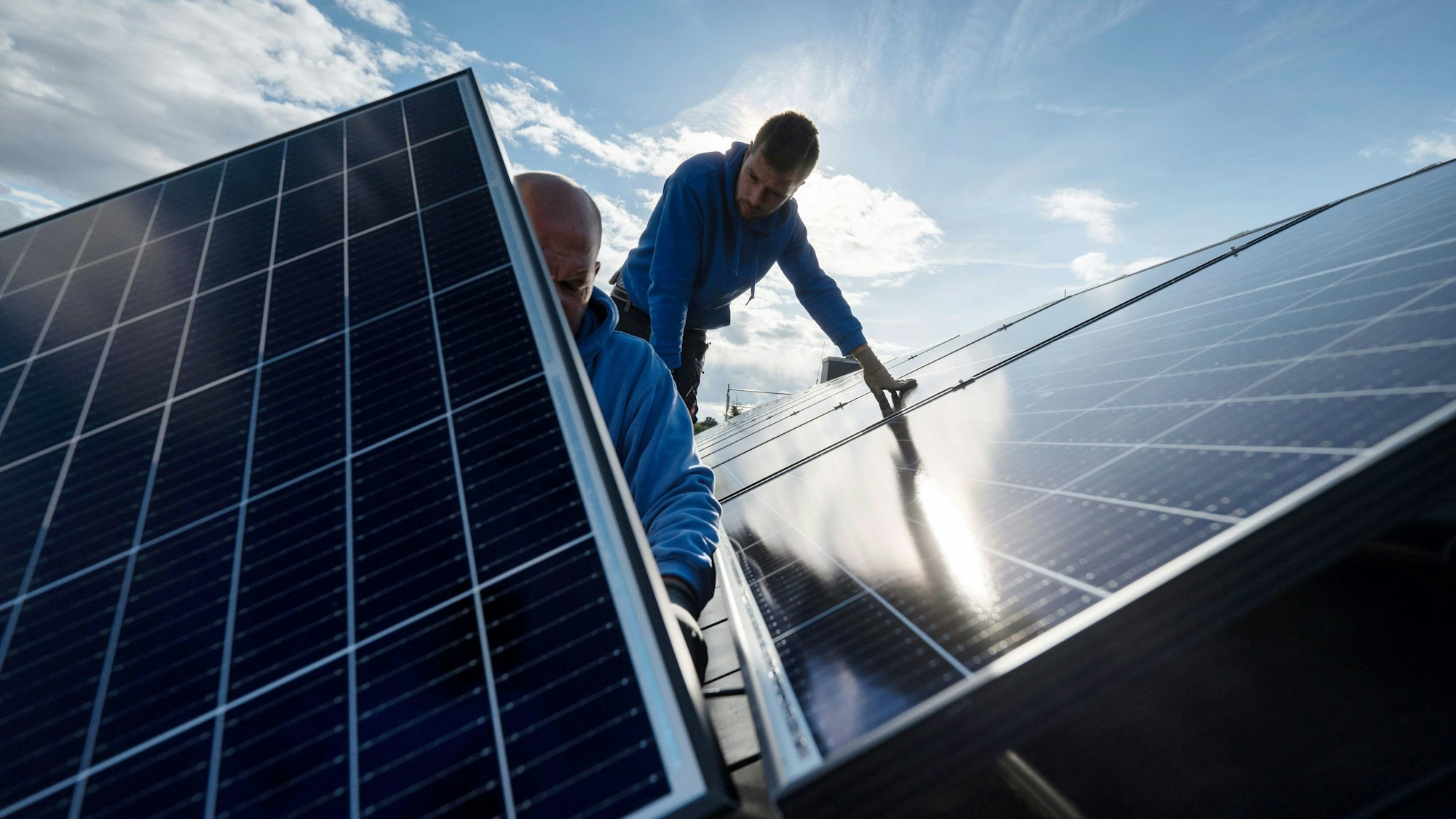 Zwei Handwerker bei der Montage von Photovoltaikmodulen auf einem Hausdach.