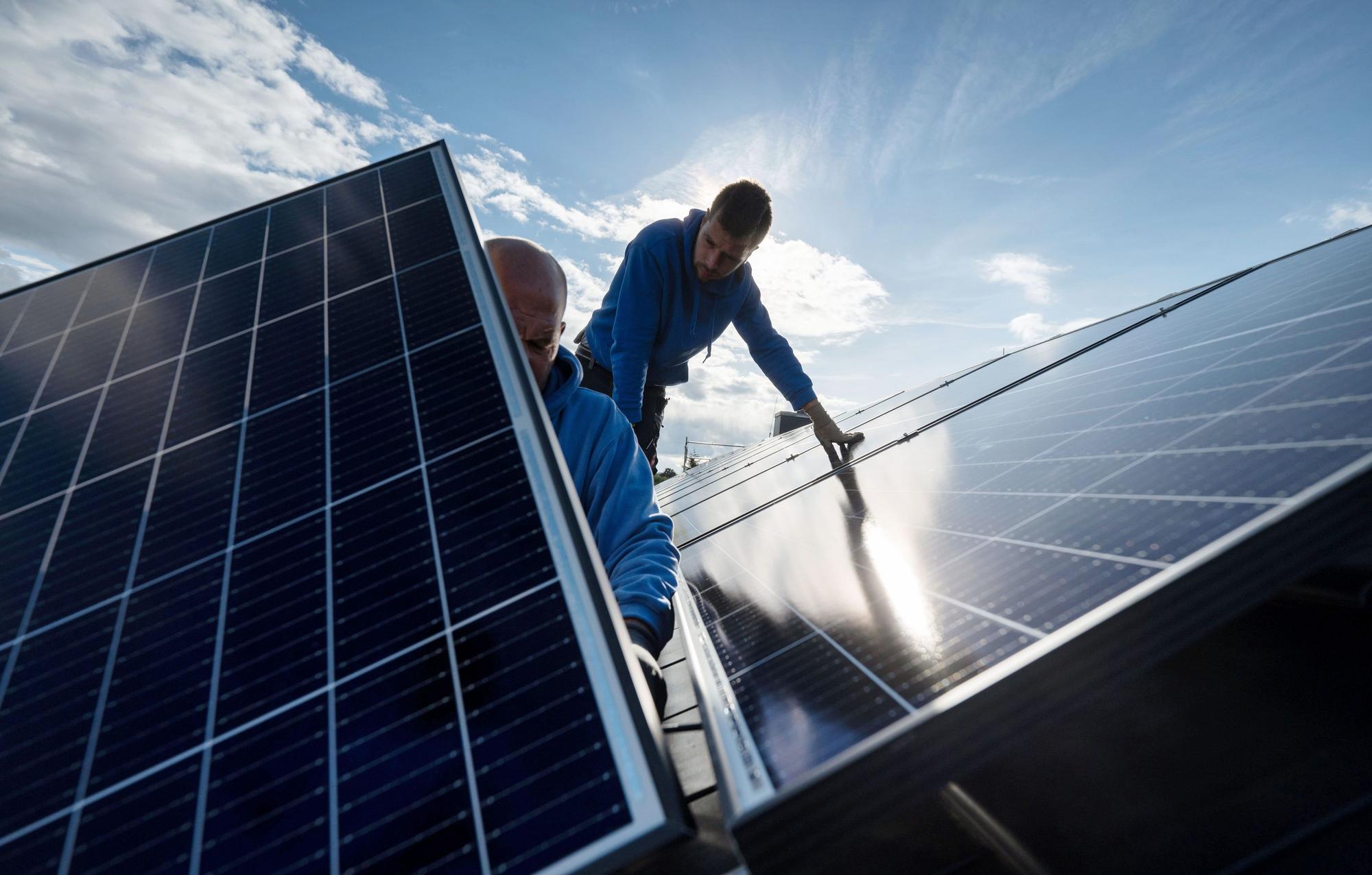 Zwei Männer montieren auf diesem Symbolbild Photovoltaikmodule auf dem Dach eines Wohnhauses.