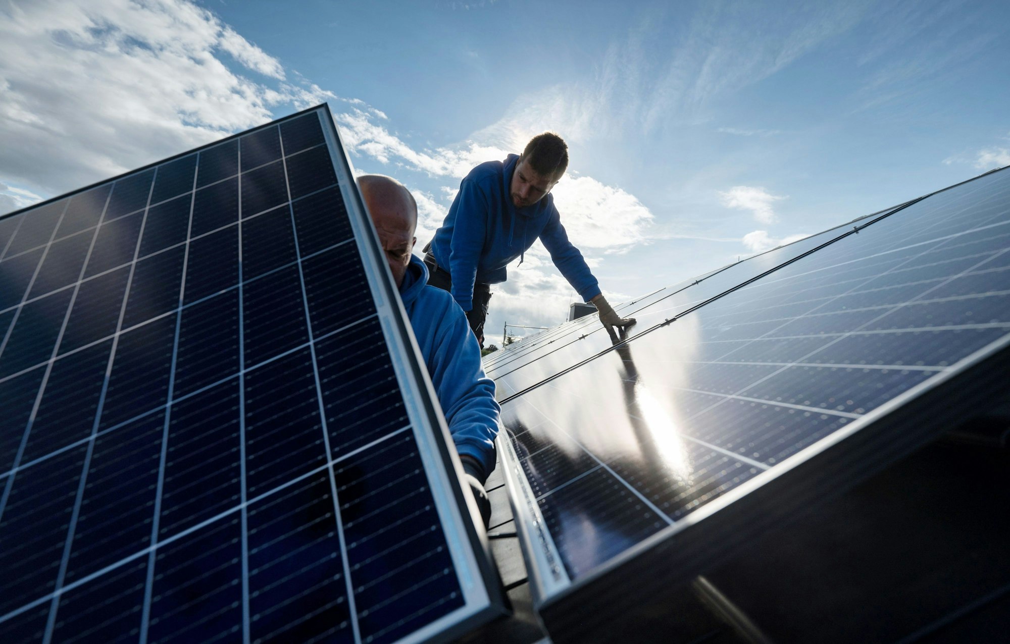 Zwei Männer montieren auf diesem Symbolbild Photovoltaikmodule auf dem Dach eines Wohnhauses.