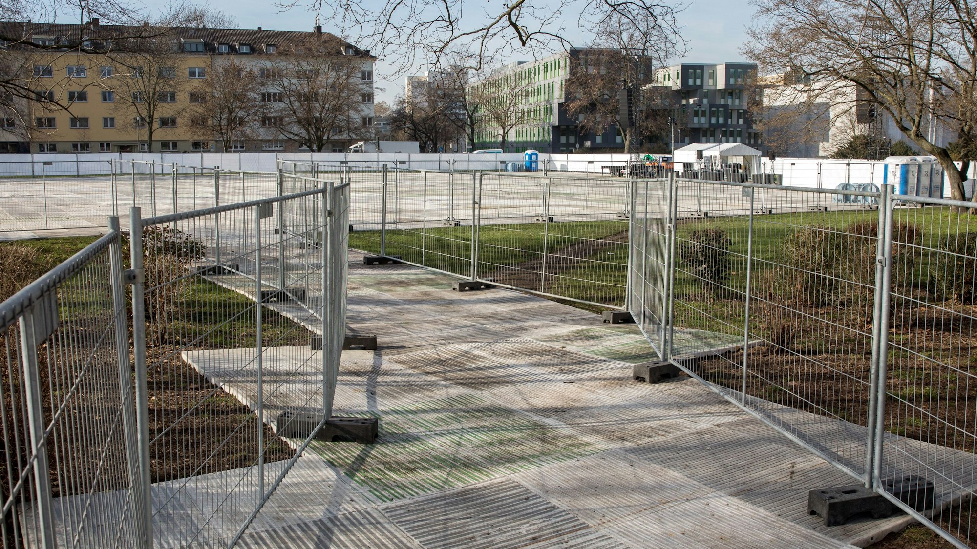 Der Blick von der Zülpicher Straße auf die Uniwiese lässt Bodenplatten und Absperrgitter erkennen, die zum Schutz der Wiese installiert wurden.