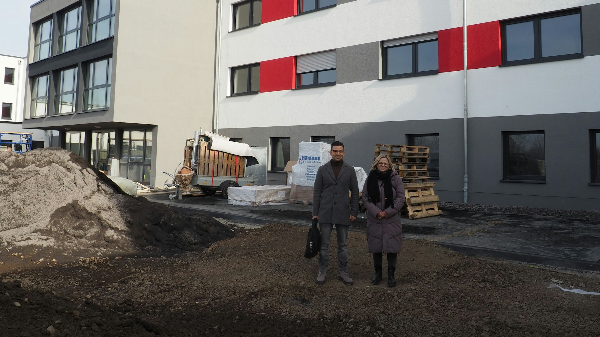 Daniel Tameh und Wiebke Herrmann stehen vor einem Gebäude auf einer Baustelle.