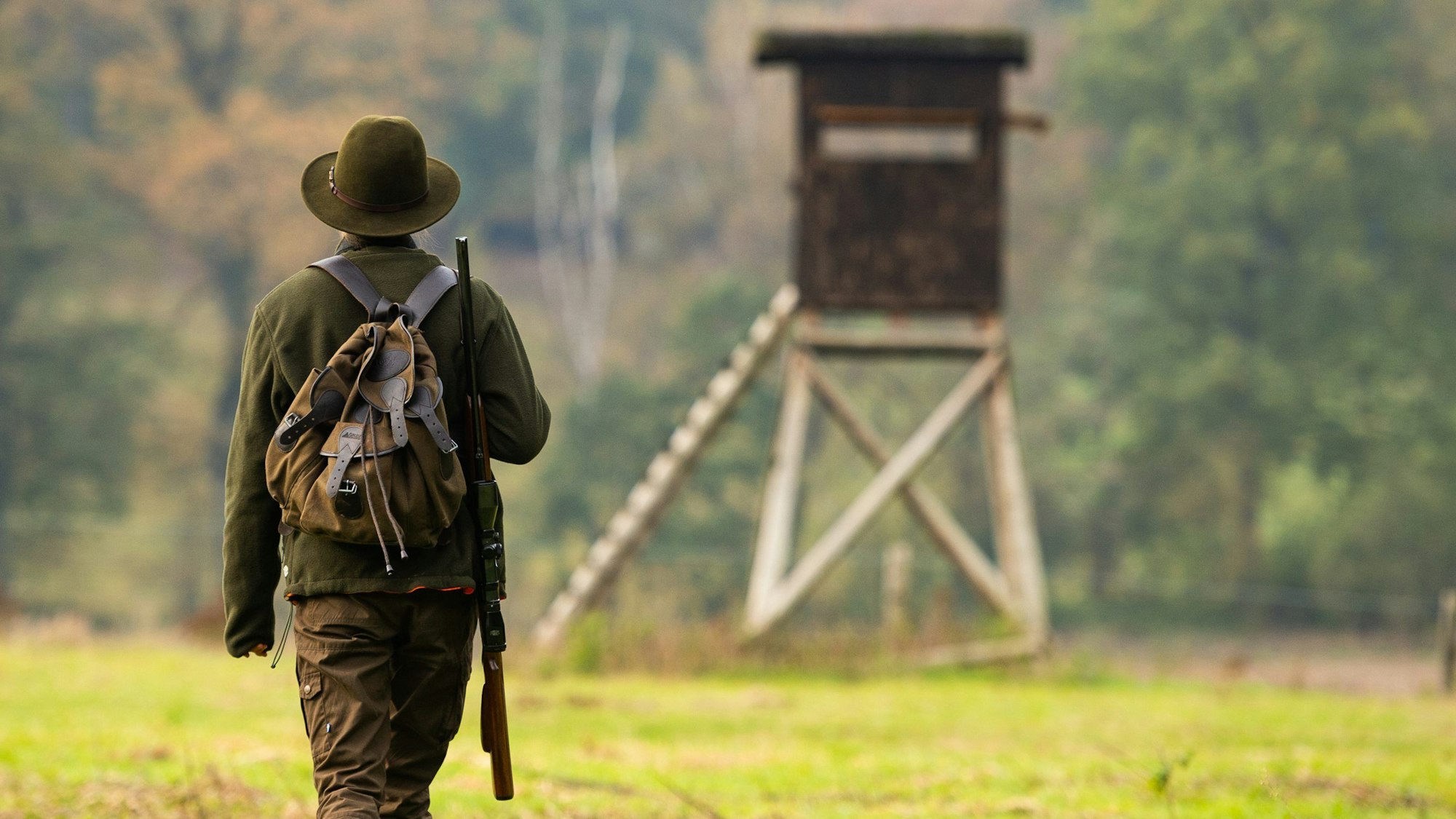 Eine Jägerin geht mit ihrer Flinte zu einem Hochsitz.