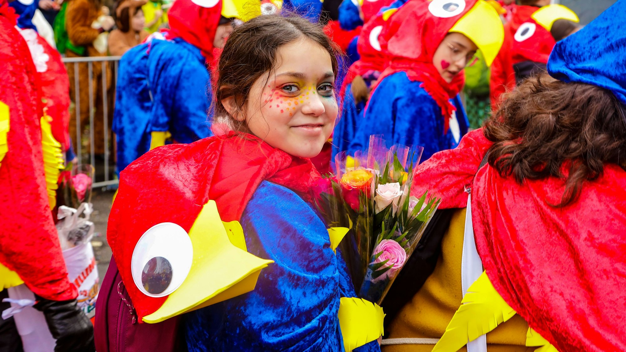 Ein Mädchen in einem Papageien-Kostüm mit Rosen in der Hand.