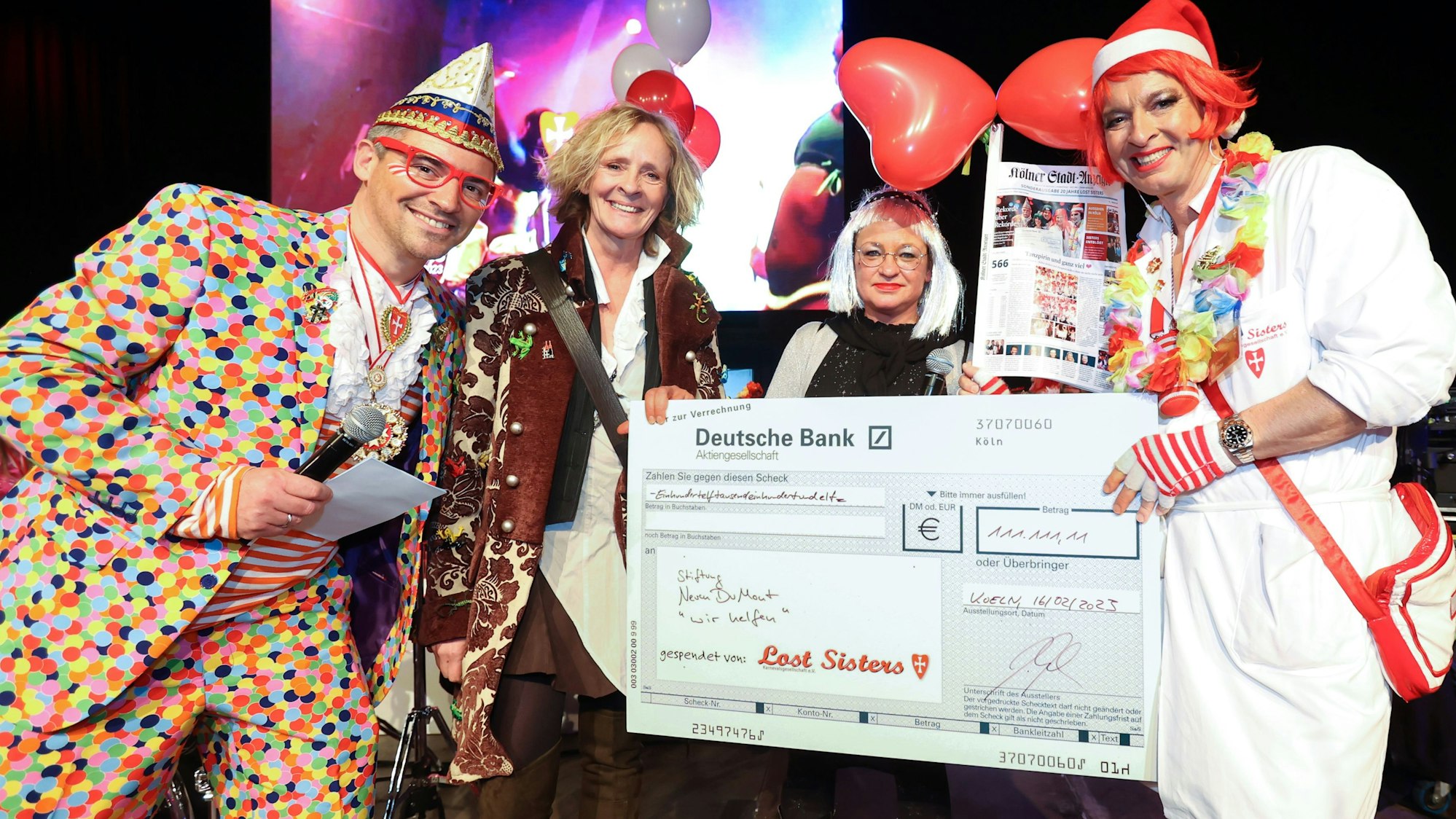 Bei der symbolischen Scheckübergabe des Kölner Karnevalsvereins „Lost Sisters“ an die Hilfsaktion des Kölner Stadt-Anzeigers für Kinder in Not, stehen der Moderator Alexander Dick im Konfetti-Anzug, Herausgeberin Isabella Neven DuMont, Redakteurin Caroline Kron als Sterntalerin und der Lost-Sisters-Vorsitzende Boris Becker im Krankenschwester-Kostüm auf der Bühne.