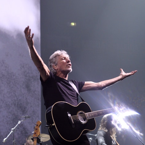 Das Bild zeigt den Musiker Rogr Waters mit einer Gitarre auf einer Bühne.
