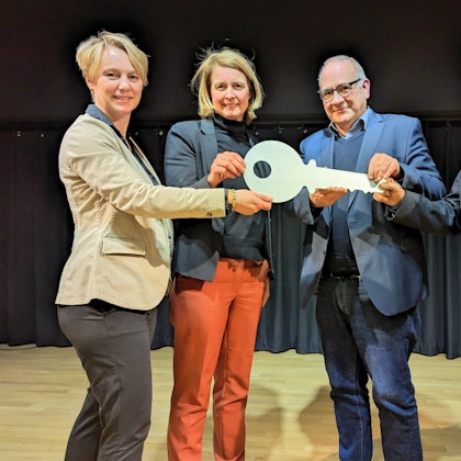 Es sind vier Menschen zu sehen, die einen großen Schlüssel in der Hand halten.