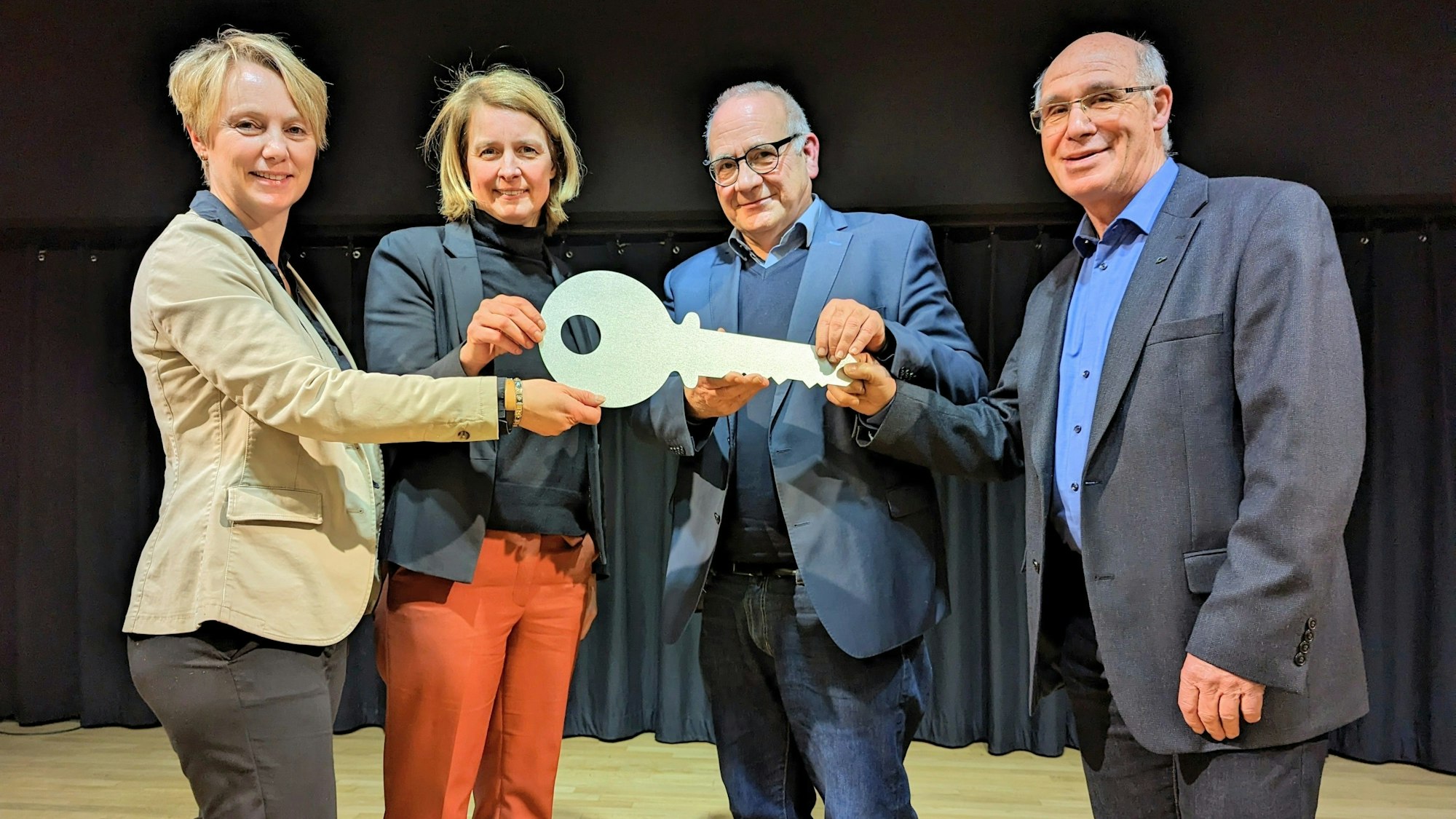 Es sind vier Menschen zu sehen, die einen großen Schlüssel in der Hand halten.