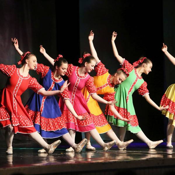 Sechs junge Mädchen in roten, blauen, gelben und grünen Kleidern zeigen einen Balletttanz.