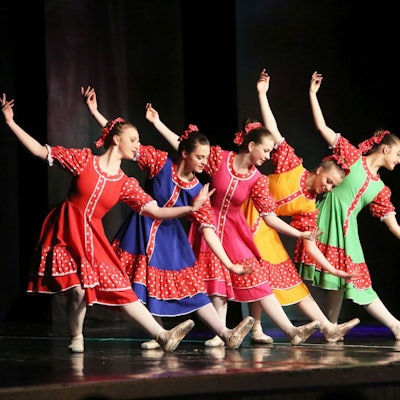 Sechs junge Mädchen in roten, blauen, gelben und grünen Kleidern zeigen einen Balletttanz.