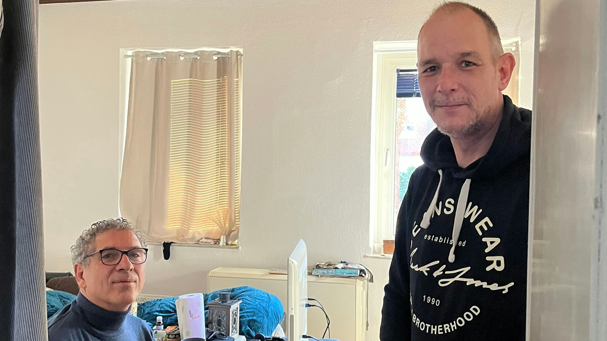 Rolf Bergheim (r.) steht in der Tür zu seinem Wohnzimmer, sitzend links ist sein Vermieter Nikos Kapourakis zu sehen.