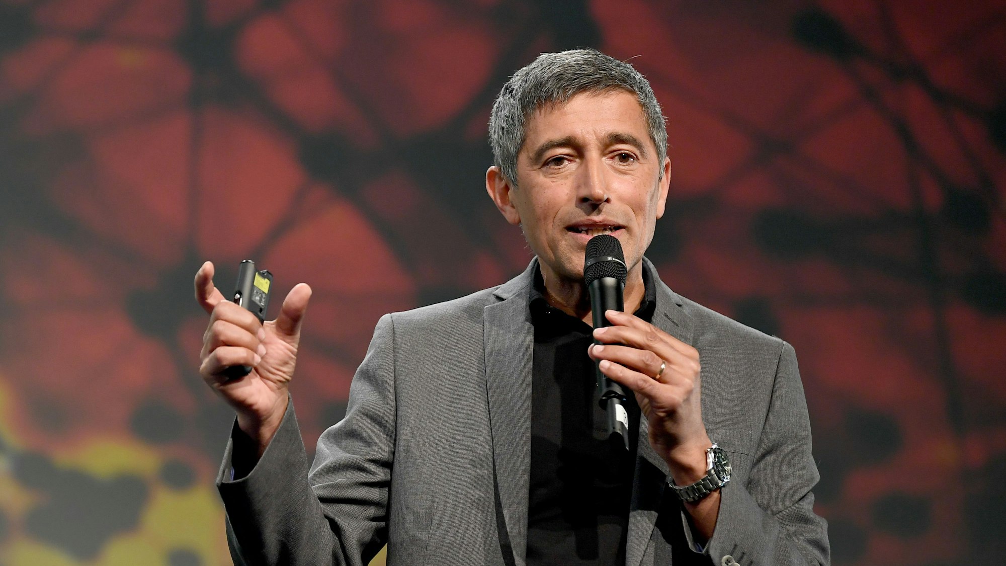 Ranga Yogeshwar trägt einen grauen Anzug, hat ein Mikrofon in der Hand, in das er spricht. Die andere Hand gestikuliert.