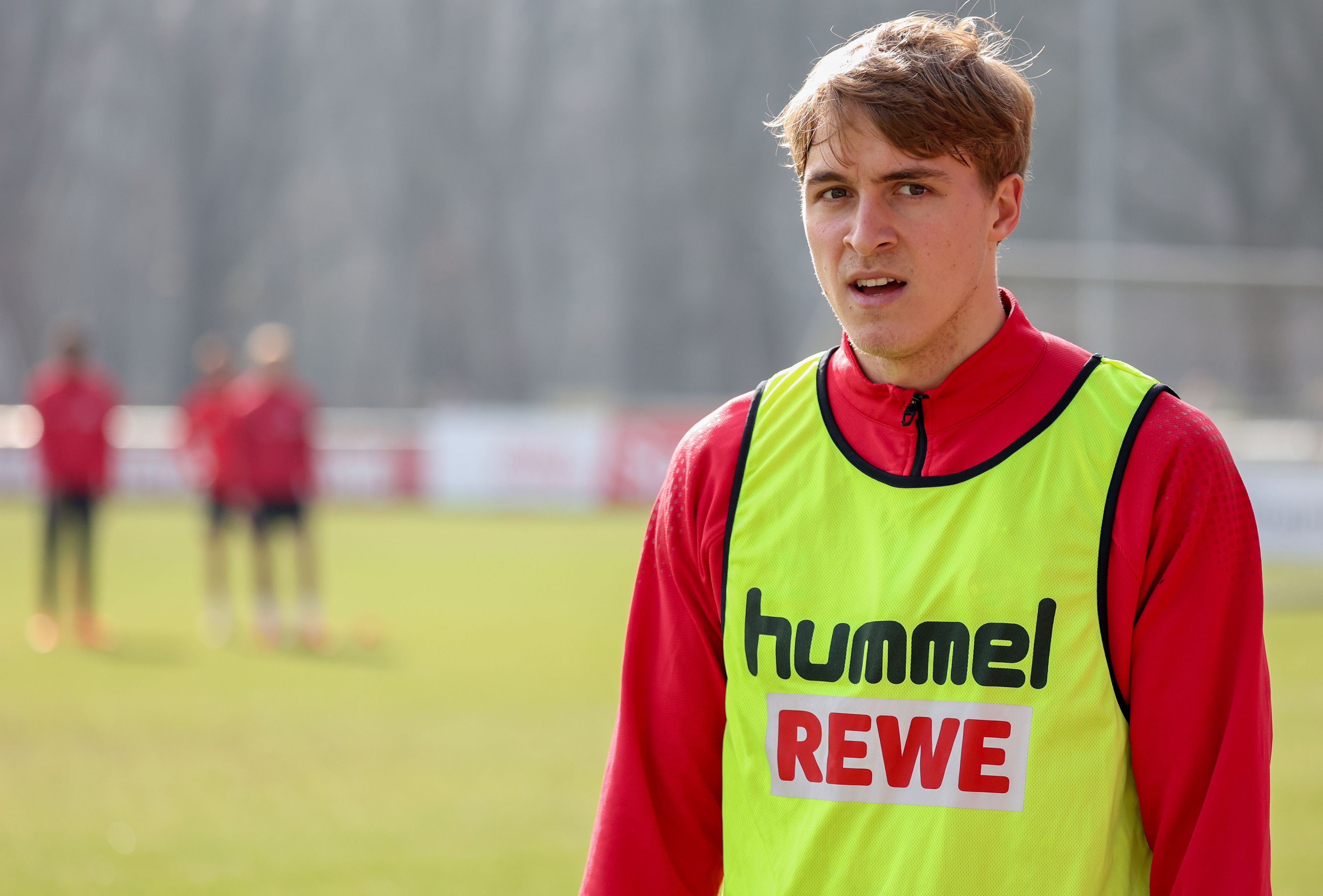 Timo Hübers am Aschermittwoch auf dem Trainingsplatz des 1. FC Köln, der Abwehrspieler trägt ein signalgelbes Trainingsleibchen zur roten Trainingsjacke.