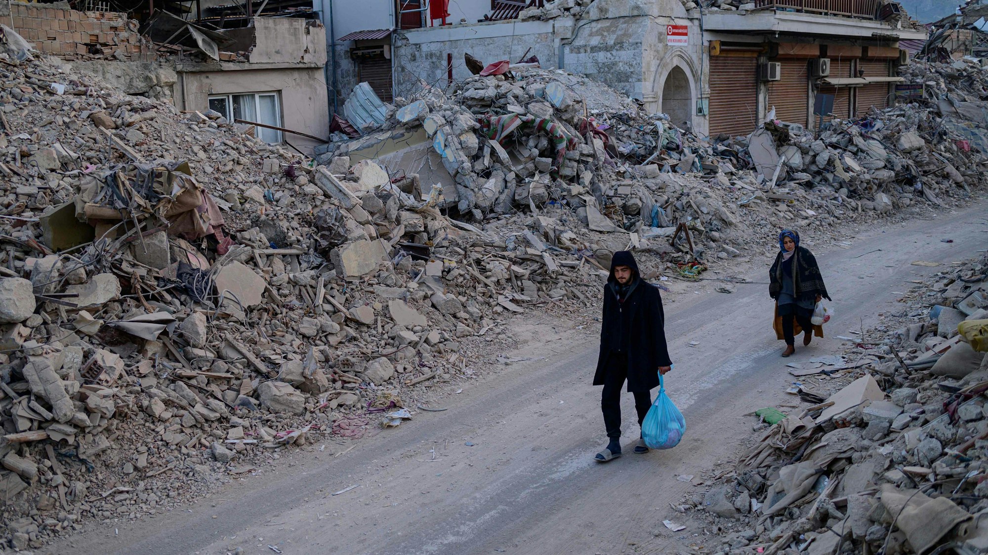 Menschen gehen an den Trümmern eingestürzter Häuser in Antakya vorbei.