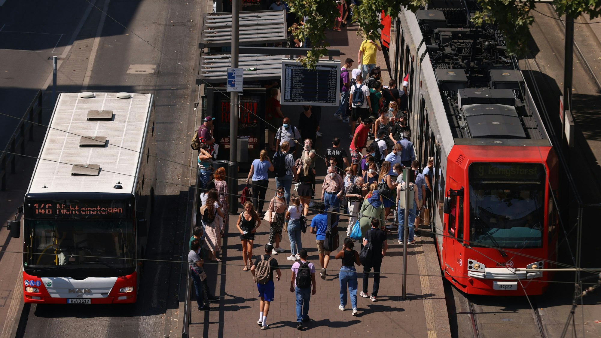 Zu sehen sind ein Bus, eine Stadtbahn und mehrere Menschen an der oberirdischen KVB-Haltestelle am Neumarkt.