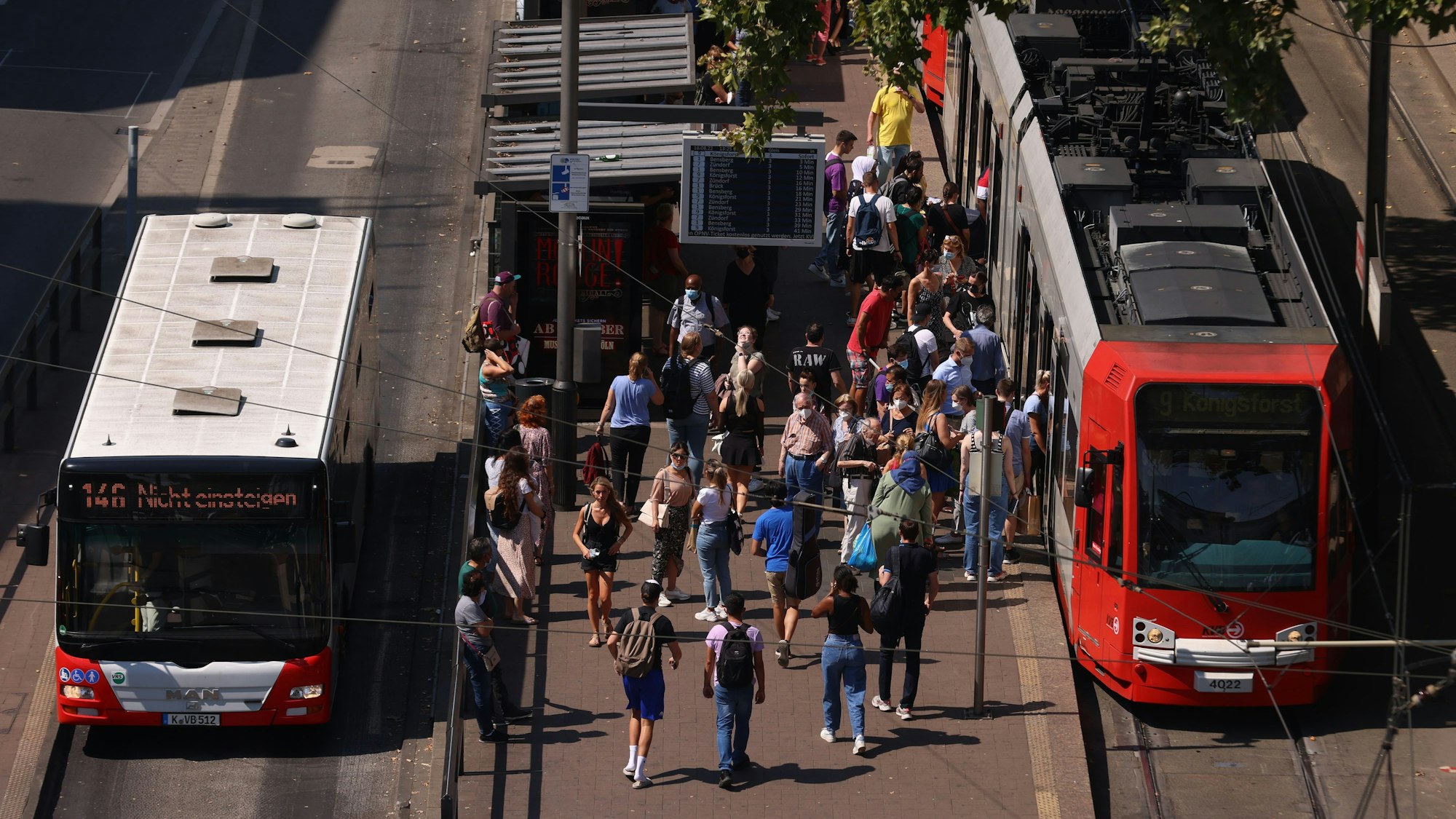 Menschen stehen an einer Bahnhaltestelle am Neumarkt, daneben eine KVB-Bahn und ein Bus.
