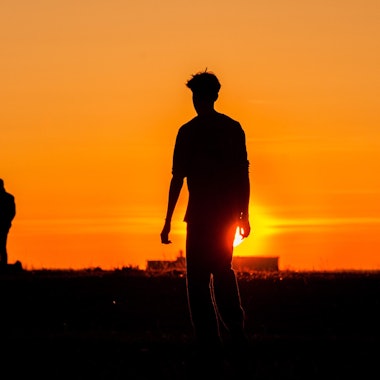Eine Gruppe Jugendlicher als Schattenrisse im Sonnenuntergang.