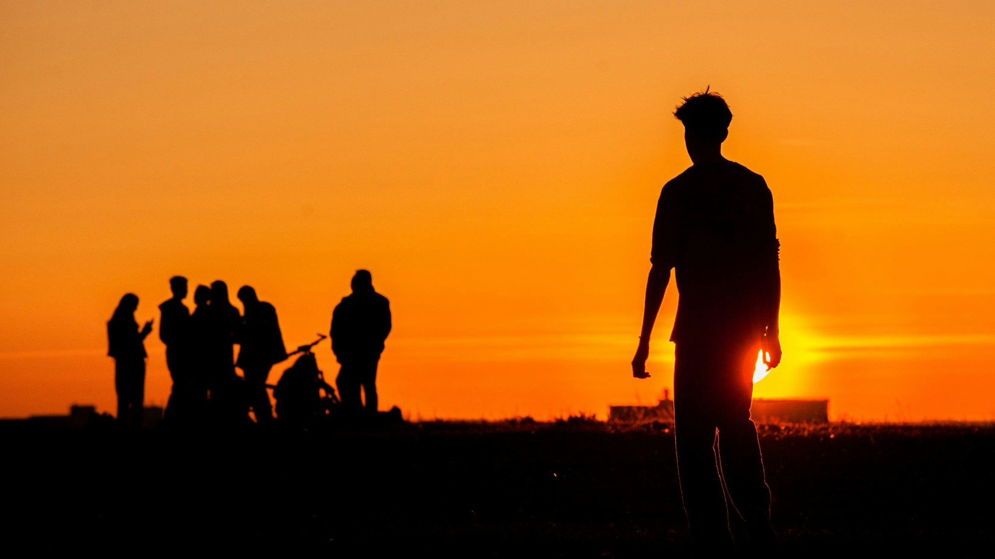 Eine Gruppe Jugendlicher als Schattenrisse im Sonnenuntergang.