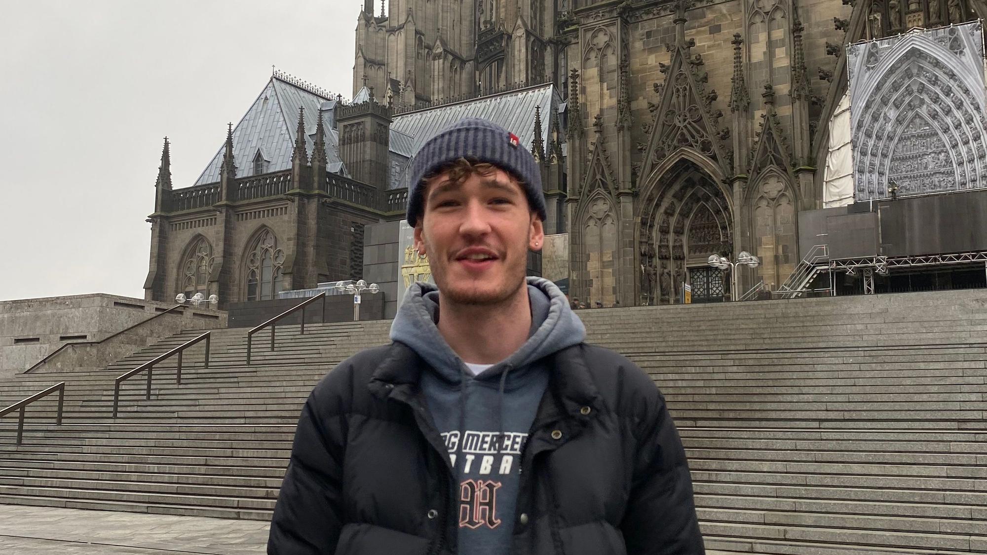 Ein junger Mann steht vor dem Kölner Dom.