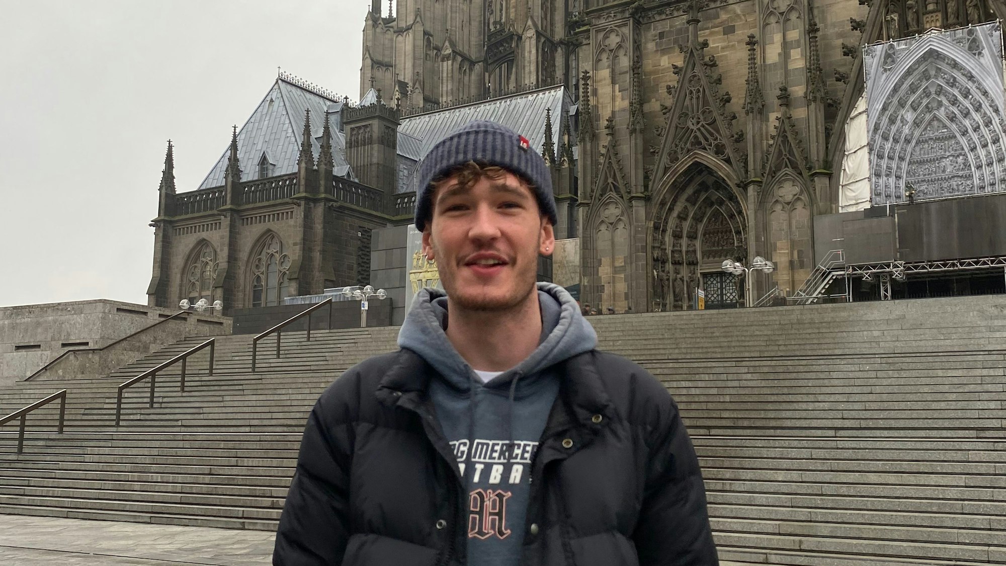 Ein junger Mann steht vor dem Kölner Dom.