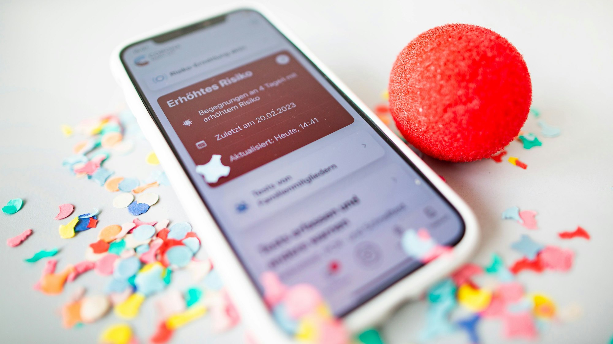 Ein Smartphone mit roter Kachel in der Corona-Warn-App liegt in Konfetti