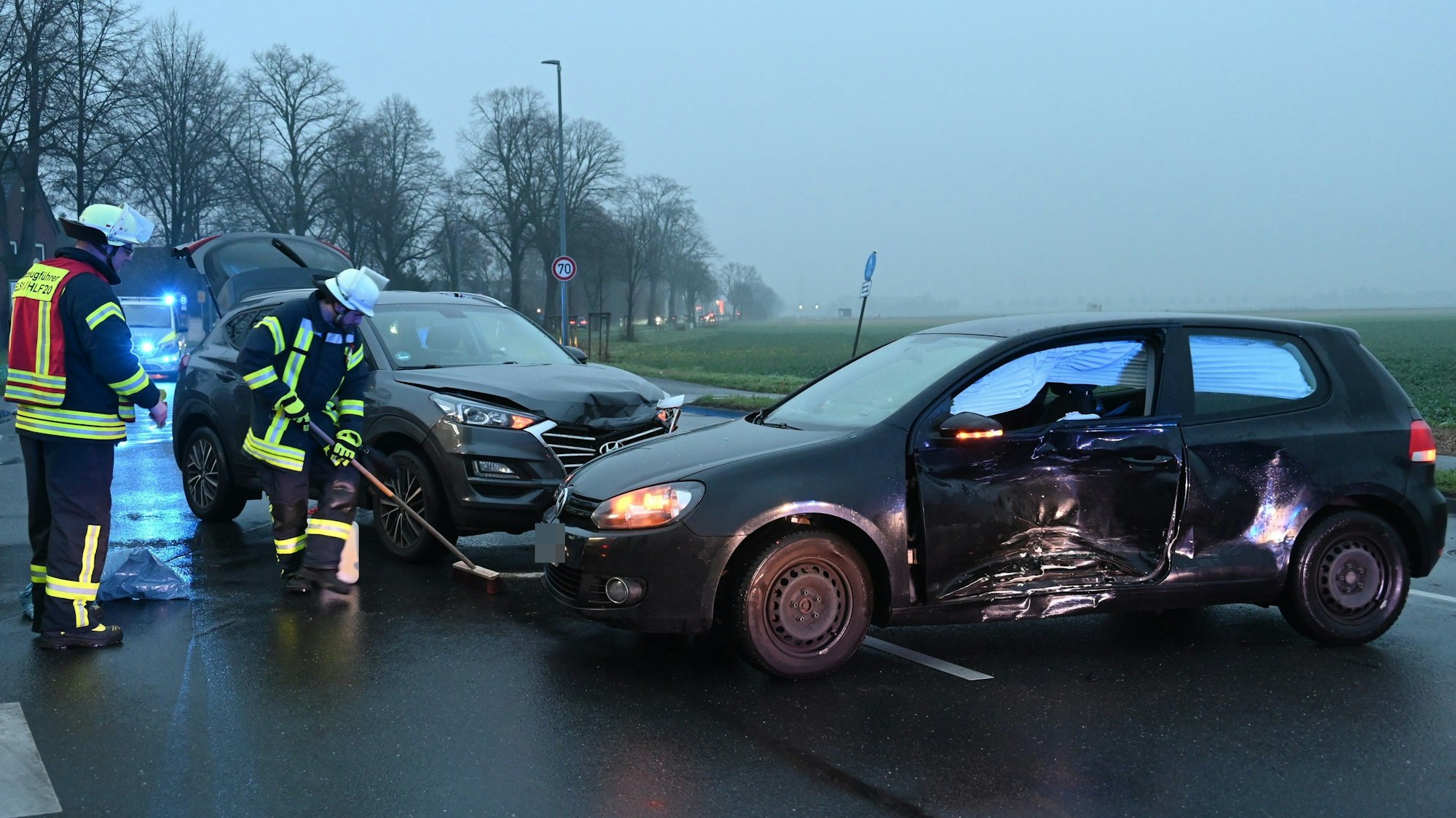 Zwei demolierte Autos stehen auf der regennassen Fahrbahn. Feuerwehrleute fegen die Fahrbahn drumherum.