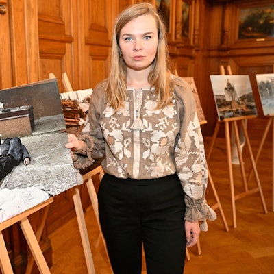 Alina Saraniuk hält ein großes Foto in der Hand. Auf dem Foto ist ein Mann zu sehen, der seinen auf der Straße erschossenen Vater findet.