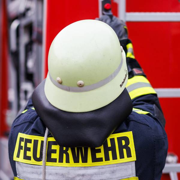 Vor einem Einsatzwagen der Feuerwehr steht eine Person der Feuerwehr.