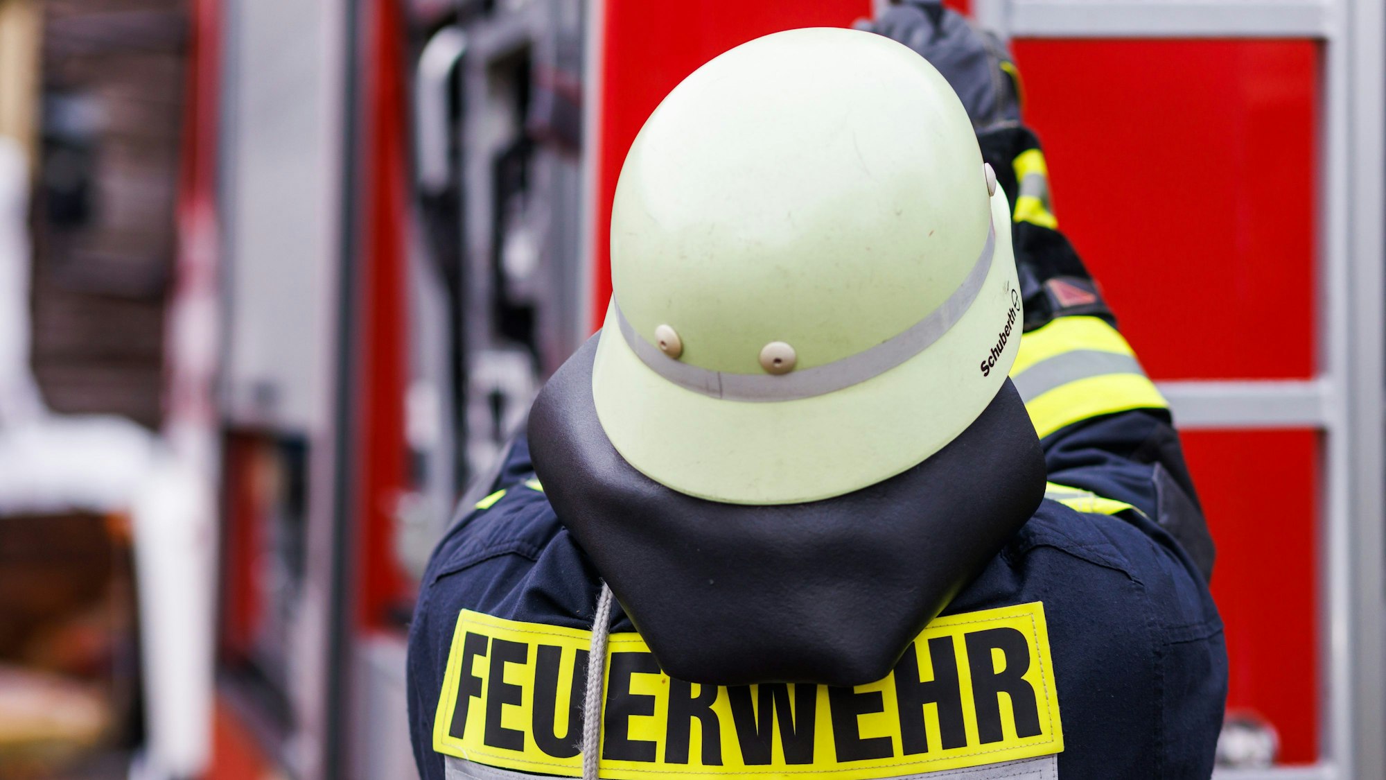 Vor einem Einsatzwagen der Feuerwehr steht eine Person der Feuerwehr.