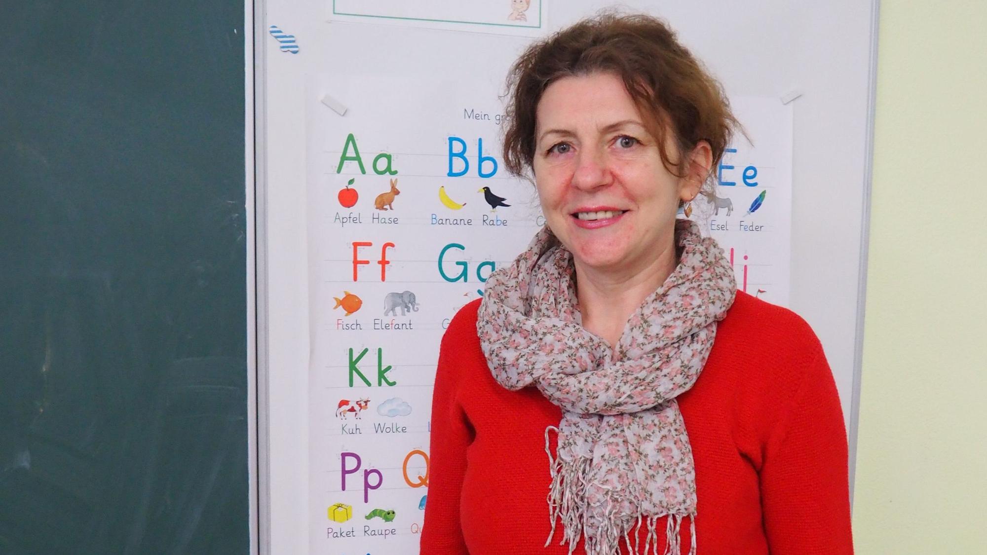 Luidmyla Yurchuk seht in rotem Pulli vor einem Plakat mit dem Alphabet.