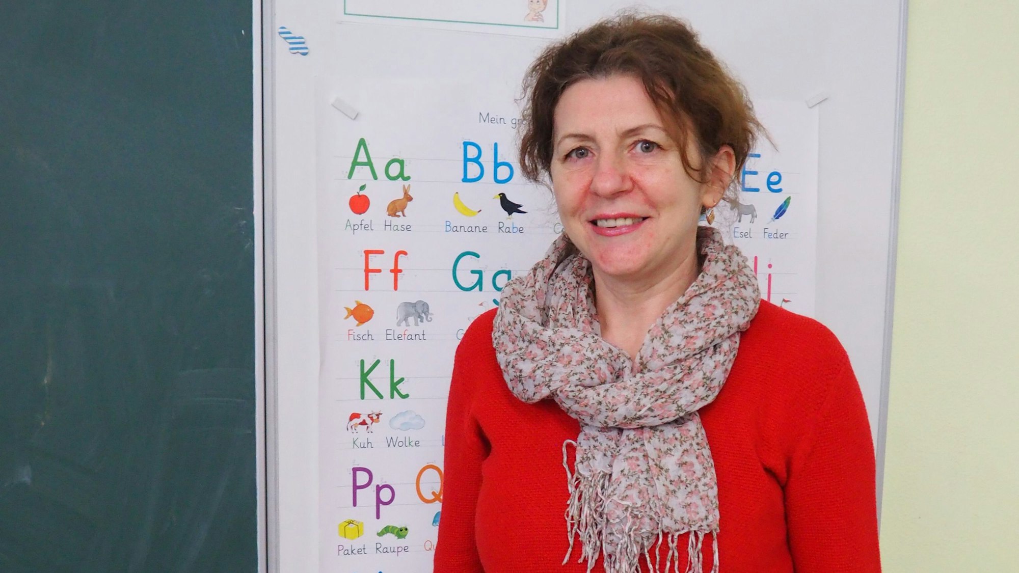 Luidmyla Yurchuk seht in rotem Pulli vor einem Plakat mit dem Alphabet.