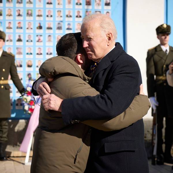 Joe Biden (Mitte r), Präsident der USA, und Wolodymyr Selenskyj, Präsident der Ukraine, umarmen sich zum Abschied an der Gedenkmauer für die gefallenen Verteidiger der Ukraine in Kiew am 20. Februar 2023. Im Hintergrund sind eine Ehrenwache ukrainischer Soldaten und ein Blumenkranz zu sehen.