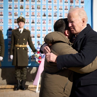 Joe Biden (Mitte r), Präsident der USA, und Wolodymyr Selenskyj, Präsident der Ukraine, umarmen sich zum Abschied an der Gedenkmauer für die gefallenen Verteidiger der Ukraine in Kiew am 20. Februar 2023. Im Hintergrund sind eine Ehrenwache ukrainischer Soldaten und ein Blumenkranz zu sehen.