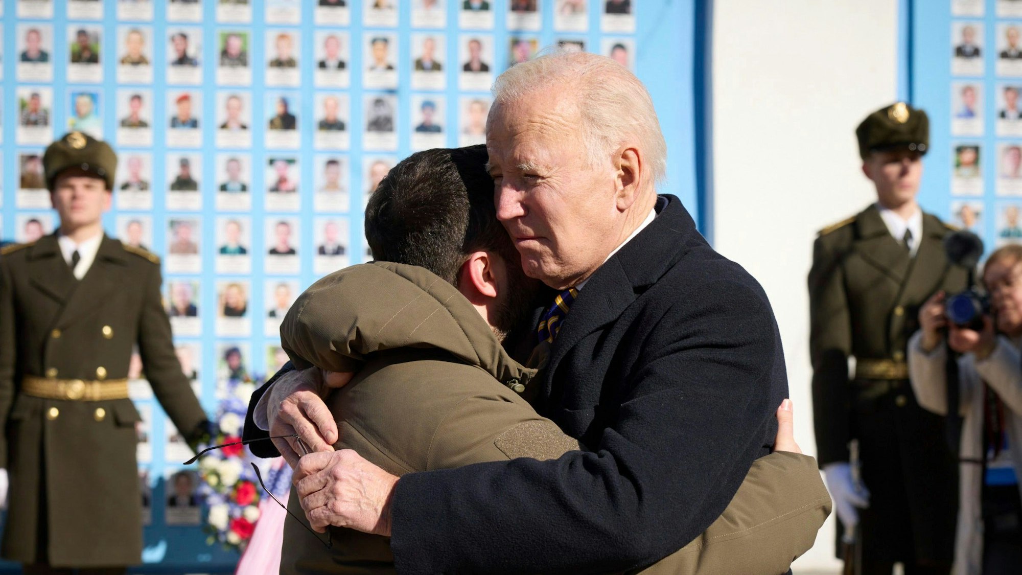 Joe Biden (Mitte r), Präsident der USA, und Wolodymyr Selenskyj, Präsident der Ukraine, umarmen sich zum Abschied an der Gedenkmauer für die gefallenen Verteidiger der Ukraine in Kiew am 20. Februar 2023. Im Hintergrund sind eine Ehrenwache ukrainischer Soldaten und ein Blumenkranz zu sehen.