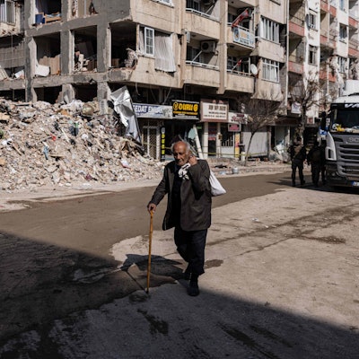 Ein Mann läuft mit einem Gehstock an durch das Erdbeben zerstörten Gebäuden vorbei. Die Trümmer liegen aufgetürmt am Straßenrand.