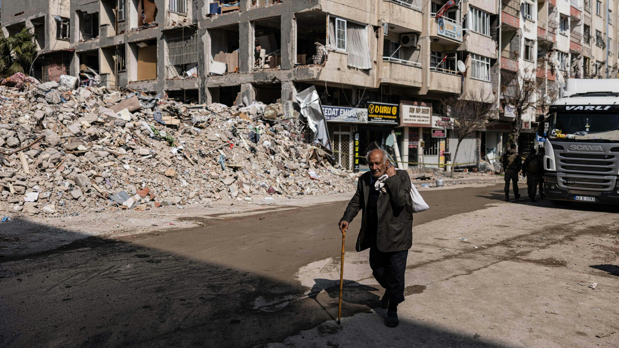 Ein Mann läuft mit einem Gehstock an durch das Erdbeben zerstörten Gebäuden vorbei. Die Trümmer liegen aufgetürmt am Straßenrand.