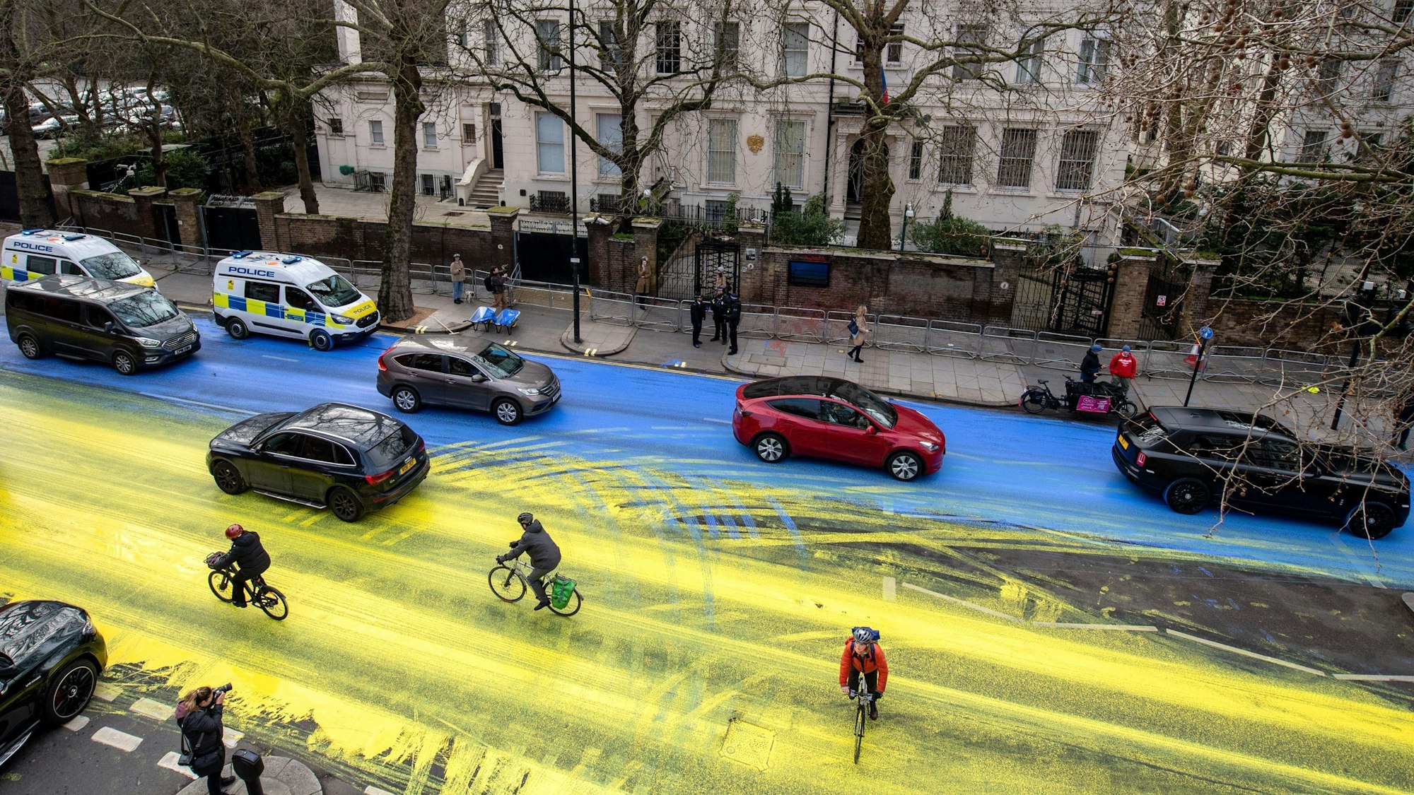London: Fahrradfahrer fahren über eine Straße vor der russischen Botschaft, die von Demonstranten in den Farben der ukrainischen Flagge angemalt wurde.