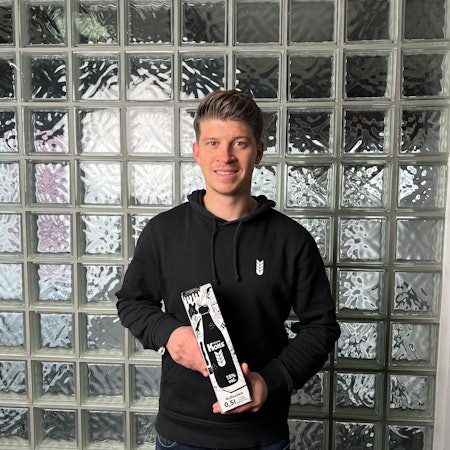 Ein junger Mann steht vor einer Glaswand.