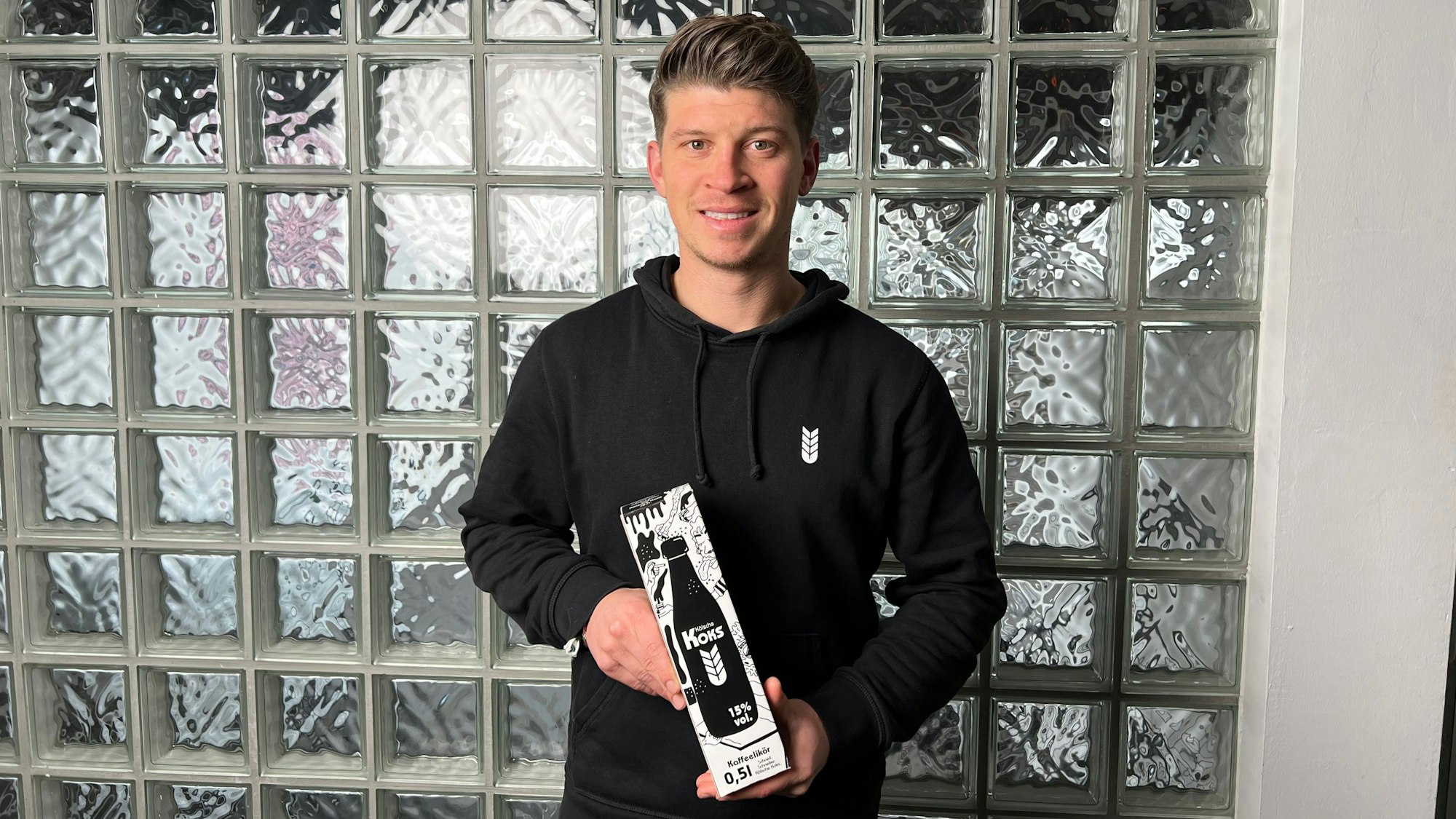 Ein junger Mann steht vor einer Glaswand.