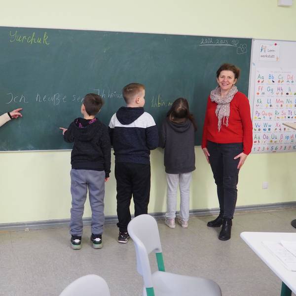 Zwei Lehrerinnen stehen an einer Tafel mit vier Kindern.