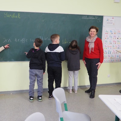 Zwei Lehrerinnen stehen an einer Tafel mit vier Kindern.