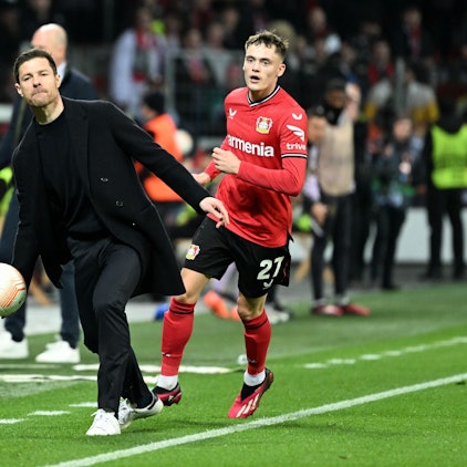 Leverkusens Trainer Xabier Alonso wirft neben Florian Wirtz einen Ball.