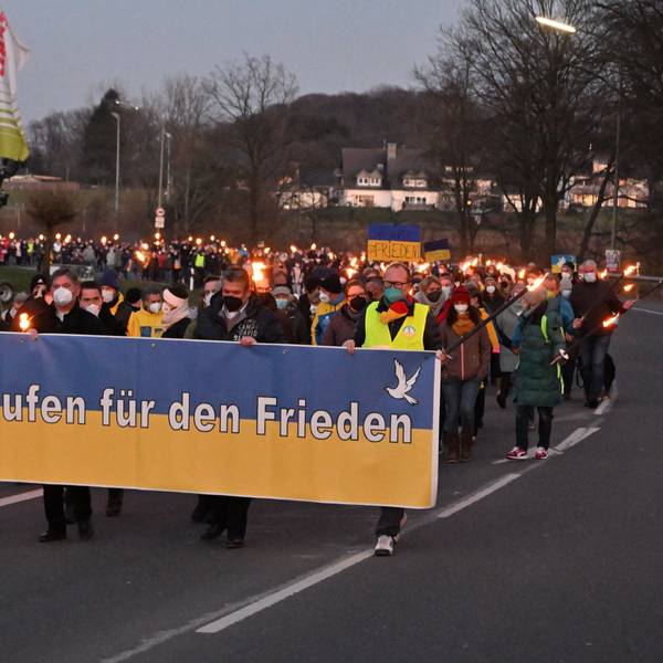 Menschen ziehen mit Fackeln und Transparenten in Kürten-Bechen eine Straße hinunter, vorne ein Banner mit der Aufschrift „Wir demonstrieren für den Frieden“.