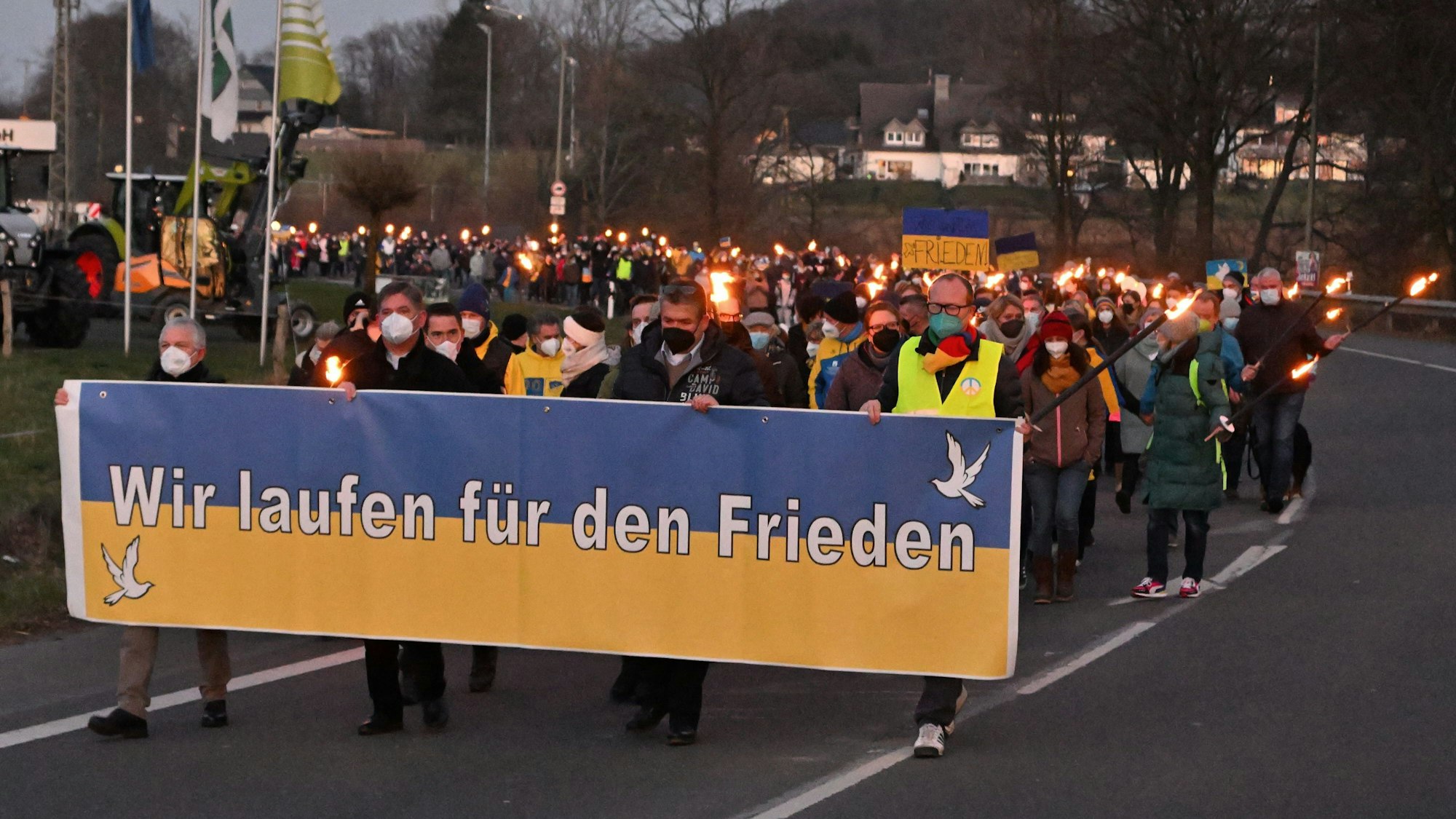 Menschen ziehen mit Fackeln und Transparenten in Kürten-Bechen eine Straße hinunter, vorne ein Banner mit der Aufschrift „Wir demonstrieren für den Frieden“.