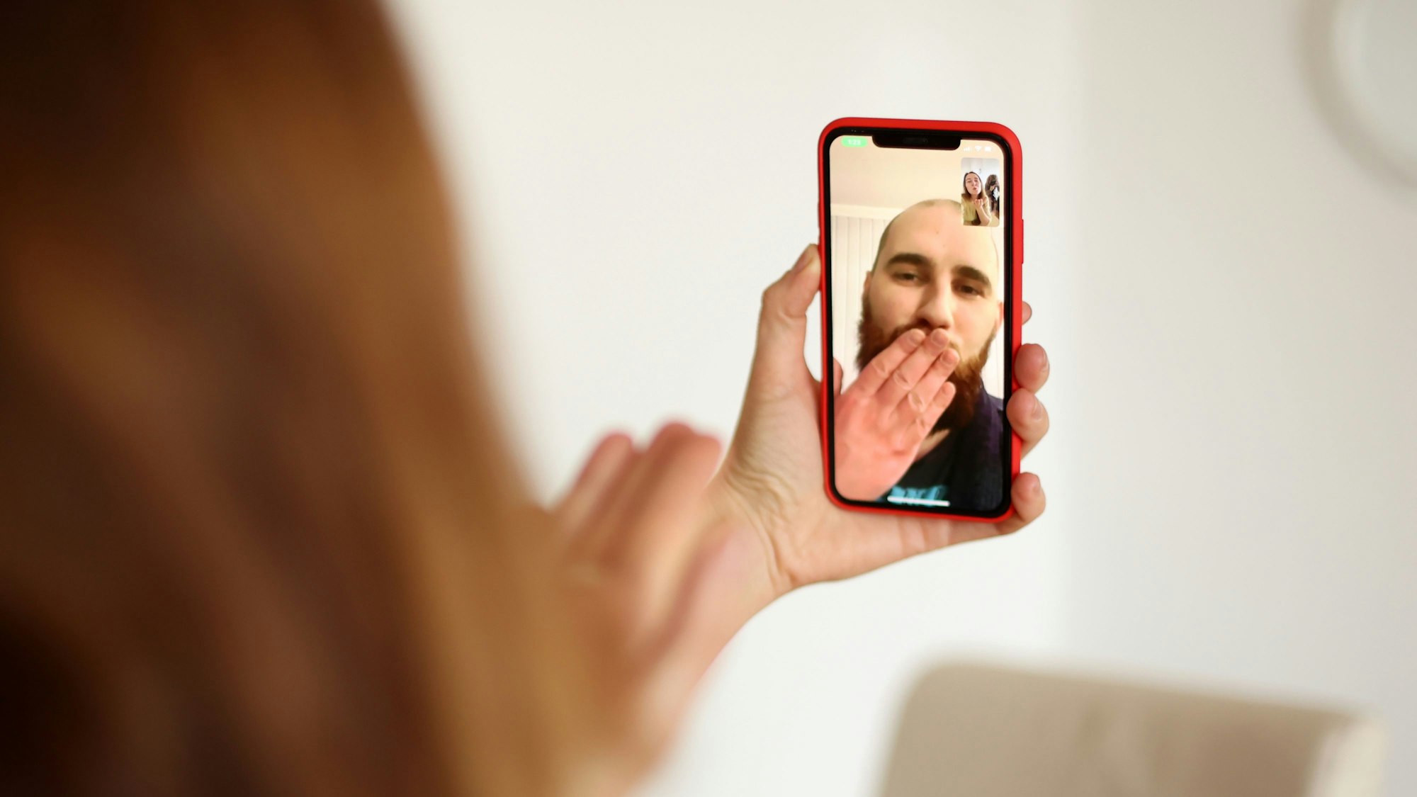 Die Kamera fokussiert an Olga vorbei auf den Bildschirm ihres Handys. Dort sieht man, wie Max seiner Frau einen Luftkuss zuwirft.